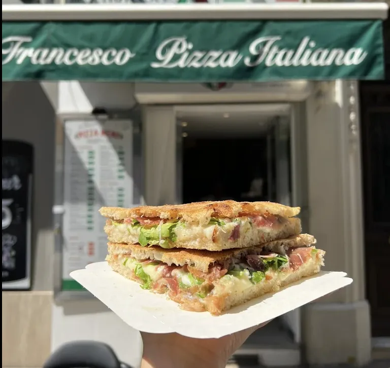 A stuffed focaccia sandwich in front of the green Da Francesco awning